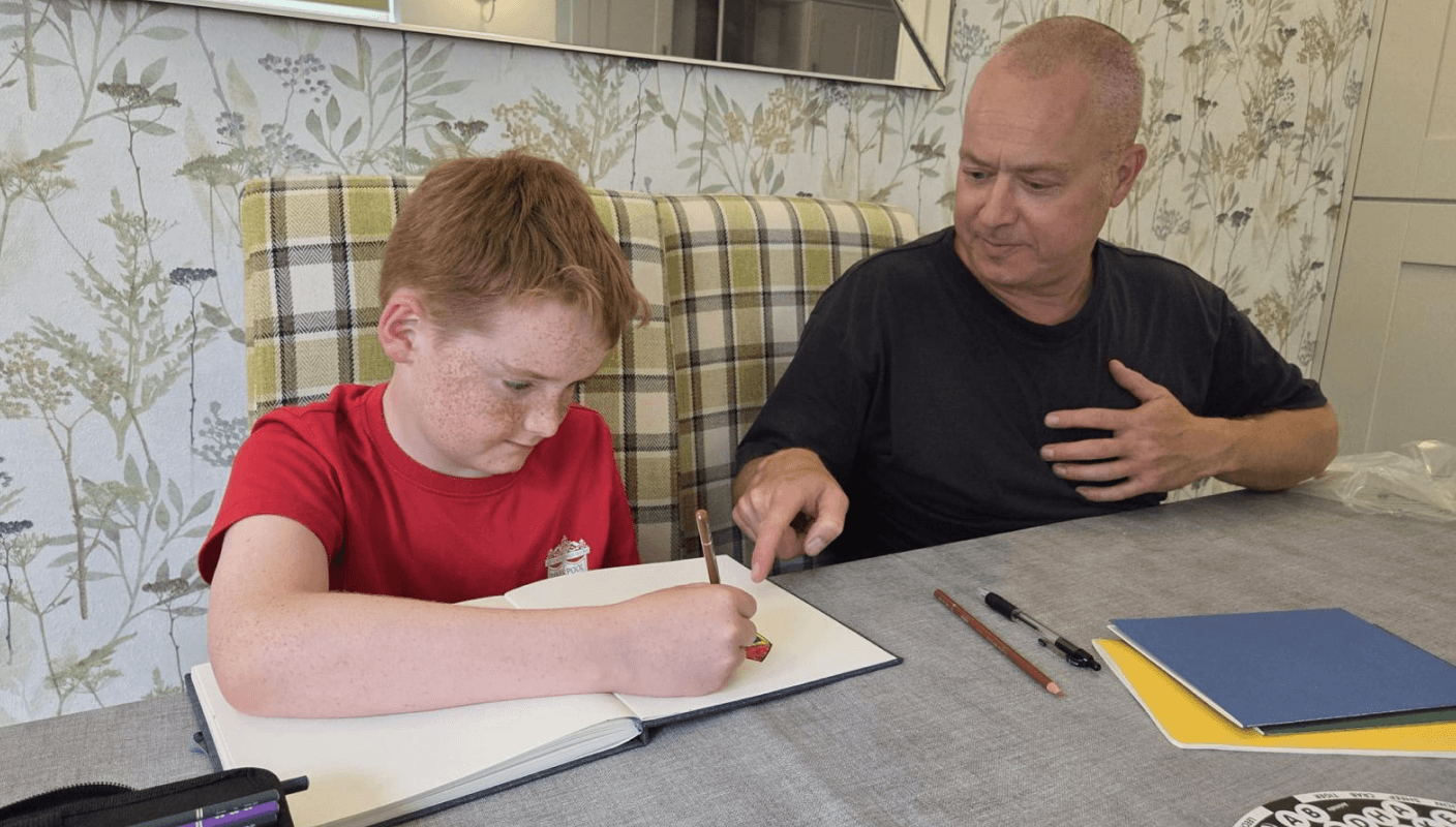 A man reading a book sitting next to child