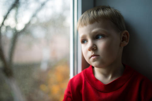 small boy sitting near window looking depressed