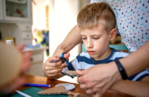 Mother helping son with dyspraxia to cut cardboard