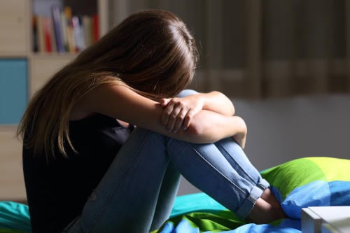 anxious teen sitting on the bed in her bedroom with a dark light in the background