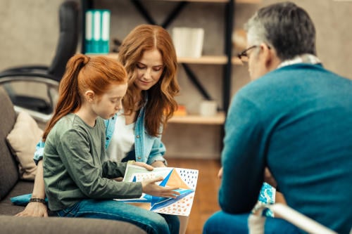 red haired girl holding a painting while describing it during autism diagnosis