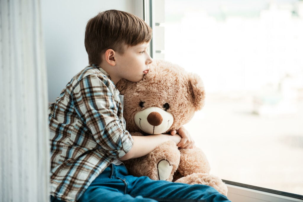 traumatised child with teddy bear sitting by the window