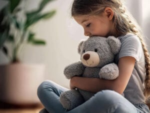 Sad child holding teddy bear suffering from trauma