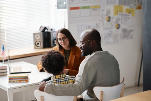 Father with child talking to teacher in classroom