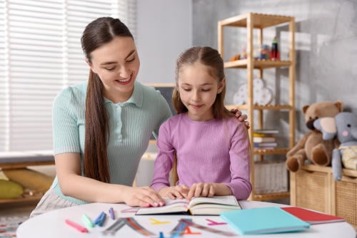 Tutor and dyslexic student reading book at table indoors