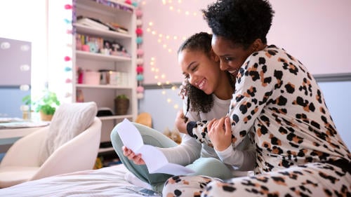 Mother With Teenage Daughter In Bedroom Looking At Letter With Positive Exam Results Together