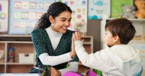 Education, teacher and child with high five in classroom for learning support, assessment success and progress pride. Happy, people and celebration at academy for development, achievement and study.