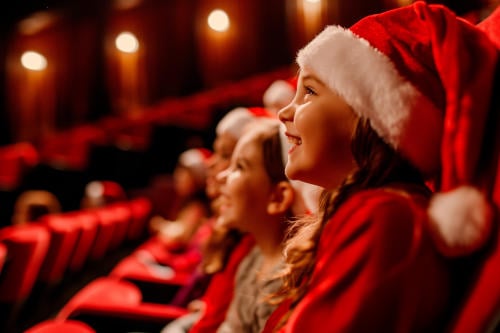 group of happy kids in santa hats watching christmas performance in a cinema