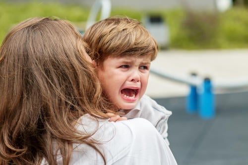 Crying child being comforted by mother outdoors