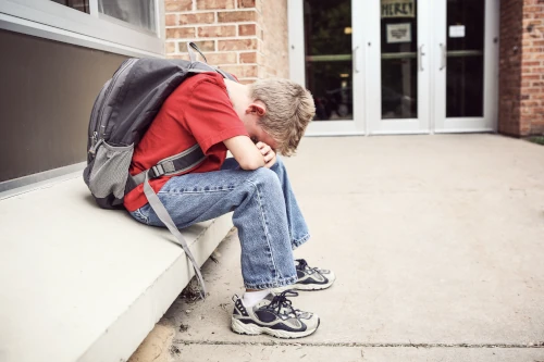 unhappy boy outside of school sitting on a bench